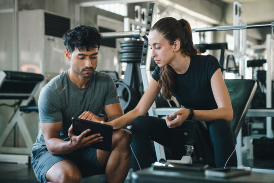 Fitness trainer athlete gym tablet coaching workout exercise health woman and man reviewing digital training plan near weight equipment