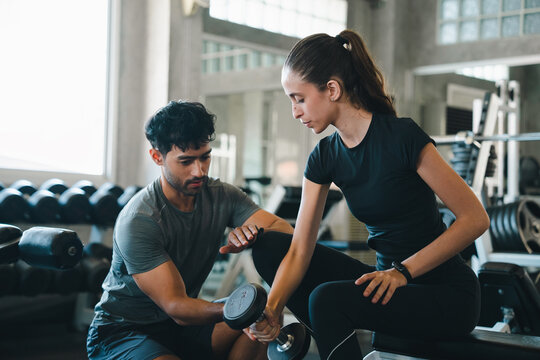Trainer woman man gym dumbbell workout fitness exercise coaching strength focused personal training session with dumbbell lift, athletic couple practicing weight exercise modern indoor health club