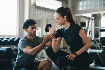 Fototapeta premium Fitness woman trainer dumbbell gym exercise coaching strength workout support, woman lifting dumbbell with male trainer guidance modern gym, focused expression during strength exercise