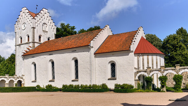 View of the historic Bosjokloster Abbey with its white stone walls, red tiled roof, and arched cloister walkways in Bosjokloster, Skane County, Sweden.