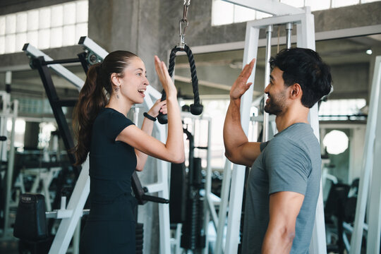 Gym woman man trainer high five fitness exercise workout strength happy High five between woman and man trainer after fitness exercise gym, with cable machine, active teamwork, motivation