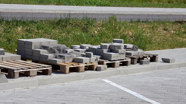 Gray interlocking concrete paving blocks arranged on wooden shipping pallets along a public sidewalk