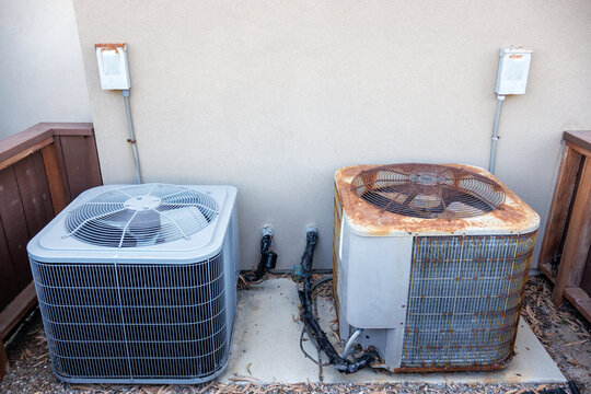 Residential HVAC setup showcasing a brand new grey air conditioner alongside a worn out old unit in enclosed  outdoor pad