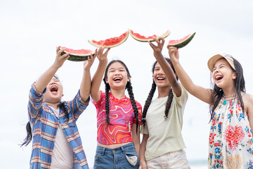 Obraz premium group of teenage friends celebrating summer break at the sea,raising watermelon slices together on a tropical beach