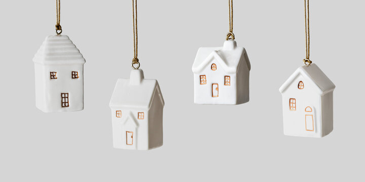 White ceramic houses ornament hanging on light gray, banner. Side view of set New Year different toys. Concept of real estate, mortgage, new home, family comfort and holiday mood, seasonal designs.