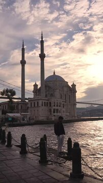 Man Walking Along Bosphorus Waterfront with Ortakoy Mosque