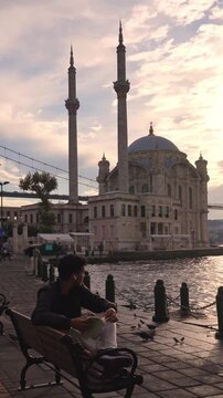 Man Relaxing on Istanbul Waterfront with Ortakoy Mosque Behind