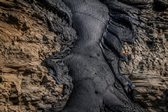 Cross-section of cooled volcanic lava flow fused with bedrock, contrasting textures.