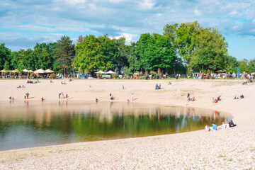 People relaxing around a small lake with a pebble beach in a green city park on a sunny spring day. Bundek lake, Zagreb, Croatia © Viktoriya
