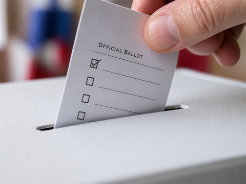 Hand placing an official ballot into a white ballot box during an election with checkboxes visible for voting rights civic duty public participation and democratic choice concept close up