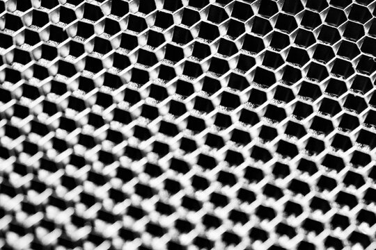 Monochrome macro shot of a shallow aluminum hexagonal grid against a shiny black backdrop