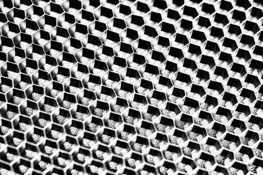 Monochrome macro shot of a shallow aluminum hexagonal grid against a shiny black backdrop