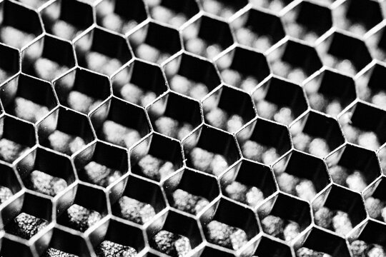 Monochrome macro shot of a shallow aluminum hexagonal grid against a shiny black backdrop