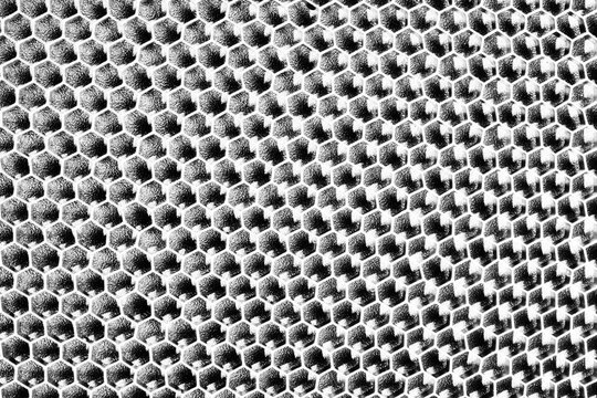 Monochrome macro shot of a shallow aluminum hexagonal grid against a shiny black backdrop