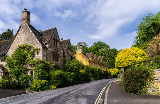 Historic village street scene in Castle Combe, Wiltshire, England. Traditional stone homes line a curved road leading to car park