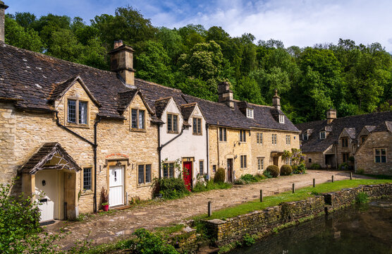 Historic Weavers Cottages reflecting in the River Bybrook, Castle Combe, Wiltshire, England on a clear day.