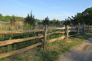 Fototapeta premium Picturesque landscape. Wooden fence along rural road in Poquott Village. Suffolk County, New York. United States