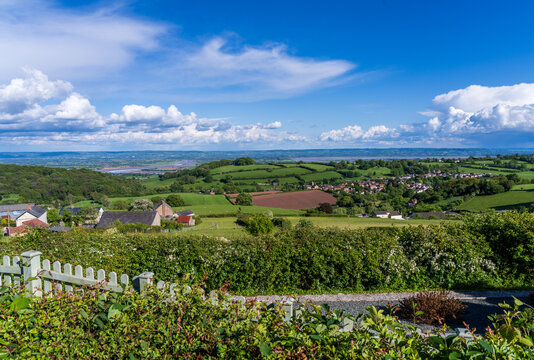 Expansive green landscape with rolling hills with Littledean in the distance with the Severn River valley under a blue sky in Gloucestershire.