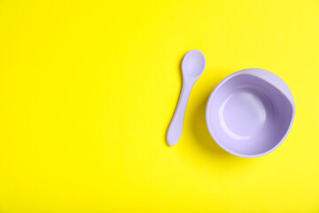 Obraz premium Baby tableware. Plastic bowl and spoon on yellow background, flat lay. Space for text