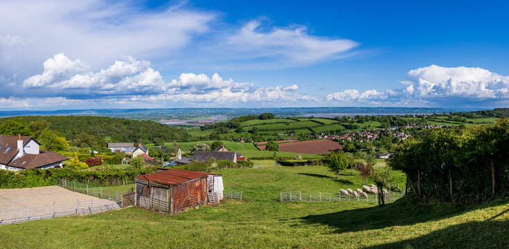 Expansive green landscape with rolling hills with Littledean in the distance with the Severn River valley under a blue sky in Gloucestershire.