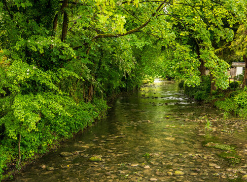 Scenic view of River Bybrook in Castle Combe, Wiltshire, England, surrounded by vibrant green trees.