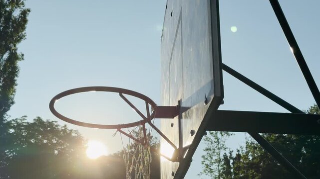 A basketball hoop stands tall against a clear blue sky in Simferopol, Crimea. The glowing morning sun creates a warm, hopeful, and nostalgic feeling over the empty court.