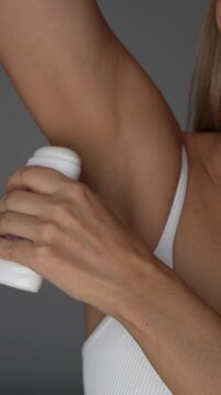 Young woman applying deodorant to her underarm, showing smooth dry skin and a simple daily hygiene routine for freshness, odor protection and comfortable body care on a grey background