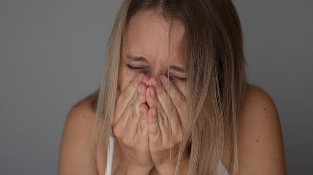 Young woman sneezing and covering her mouth and nose with both hands, showing cold or allergy symptoms indoors in a close-up portrait about hygiene, illness and seasonal health care