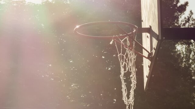 A basketball hoop glows under warm, hazy sunlight. This nostalgic view evokes a sense of peaceful longing and pure joy. Green trees stand quietly in the background.