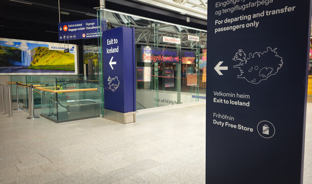Keflavik airport terminal displaying an exit to iceland sign and a large welcoming skogafoss waterfall mural with escalators