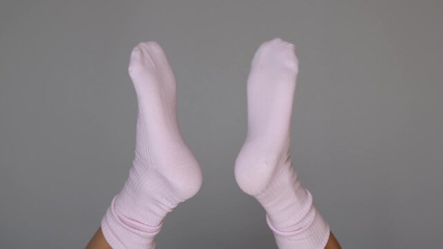 Playful female feet in pink socks clap together like hands, creating a funny quirky gesture and a lighthearted mood on a grey background