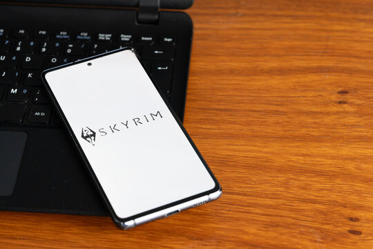Punta Arenas, Chile &ndash; July 2, 2026: The Skyrim video game logo displayed on a smartphone screen resting on a laptop keyboard over a wooden table background
