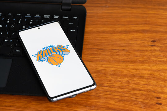 Punta Arenas, Chile &ndash; July 3, 2026: The New York Knicks logo displayed on a smartphone screen resting on a laptop keyboard over a wooden table background