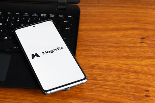Punta Arenas, Chile &ndash; July 6, 2026: The Magnific AI by Freepik application logo displayed on a smartphone screen resting on a laptop keyboard over a wooden table background