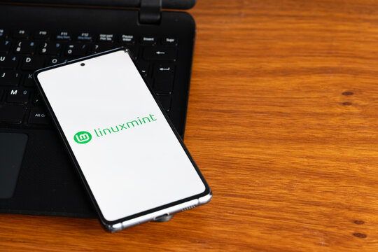 Punta Arenas, Chile &ndash; July 6, 2026: The Linux Mint operating system logo displayed on a smartphone screen resting on a laptop keyboard over a wooden table background