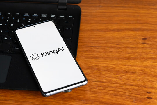 Punta Arenas, Chile &ndash; July 6, 2026: The Kling AI application logo displayed on a smartphone screen resting on a laptop keyboard over a wooden table background