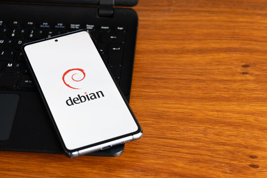 Punta Arenas, Chile &ndash; July 8, 2026: The Debian Linux operating system logo displayed on a smartphone screen resting on a laptop keyboard over a wooden table background