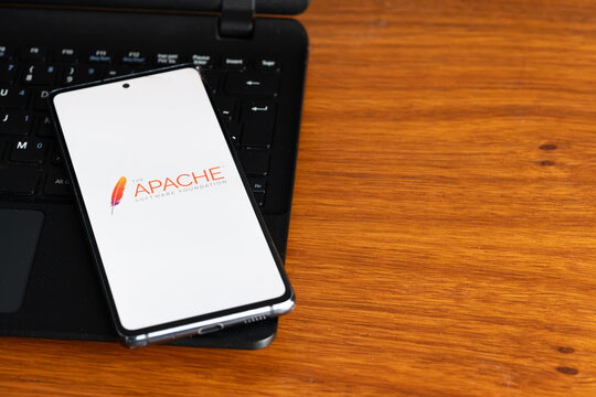 Punta Arenas, Chile &ndash; July 8, 2026: The Apache Software Foundation logo displayed on a smartphone screen resting on a laptop keyboard over a wooden table background