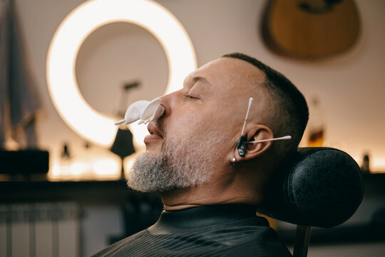 Male client in barbershop with relaxing treatment, ear and nose hair removal waxing