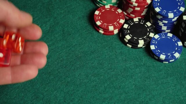 Hand rolls two dice across a green felt table surrounded by colorful poker chips in a gaming environment