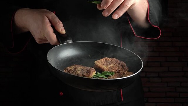 Chef sprinkles fresh herbs over sizzling meat in a frying pan, steam rising in a dimly lit kitchen with brick wall background