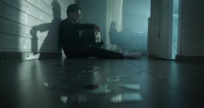 Depressed man sit floor drink bottle alcohol, angry woman ignore. Domestic conflict, relationship crisis. Alco addiction concept. Couple arguing dark room home. Quarrel people separation bad break up.