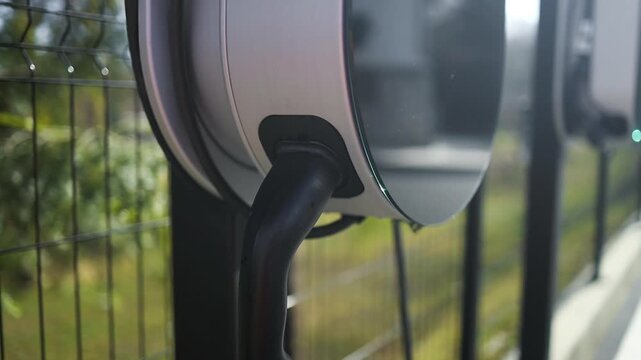close-up shot of a modern EV home charging station wallbox with a wrapped cable, mounted on a pole outdoors next to a private house backyard.