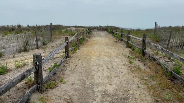 Tilt down view of a sandy path to the beach with a spit rail wooden fence