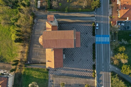 Aerial view of the church in Chiesanuova with its red-tiled roof and patterned stone courtyard, situated next to a road with a crosswalk in Chiesanuova, Chiesanuova, San Marino.