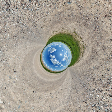creative tiny planet photo of a rural landscape with dirt road, green fields, and cloudy sky forming a circular world.