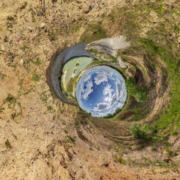 creative tiny planet photo of a rural landscape with dirt road, green fields, and cloudy sky forming a circular world.