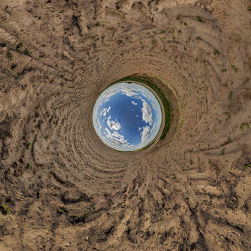 creative tiny planet photo of a rural landscape with dirt road, green fields, and cloudy sky forming a circular world.