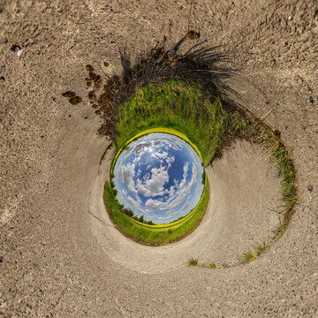 creative tiny planet photo of a rural landscape with dirt road, green fields, and cloudy sky forming a circular world.