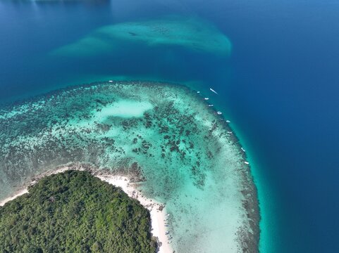 Aerial view of Ko Phai island with turquoise coral reefs, clear blue water, and small boats anchored near the white sandy beach in Bang Lamung District, Chon Buri, Thailand.